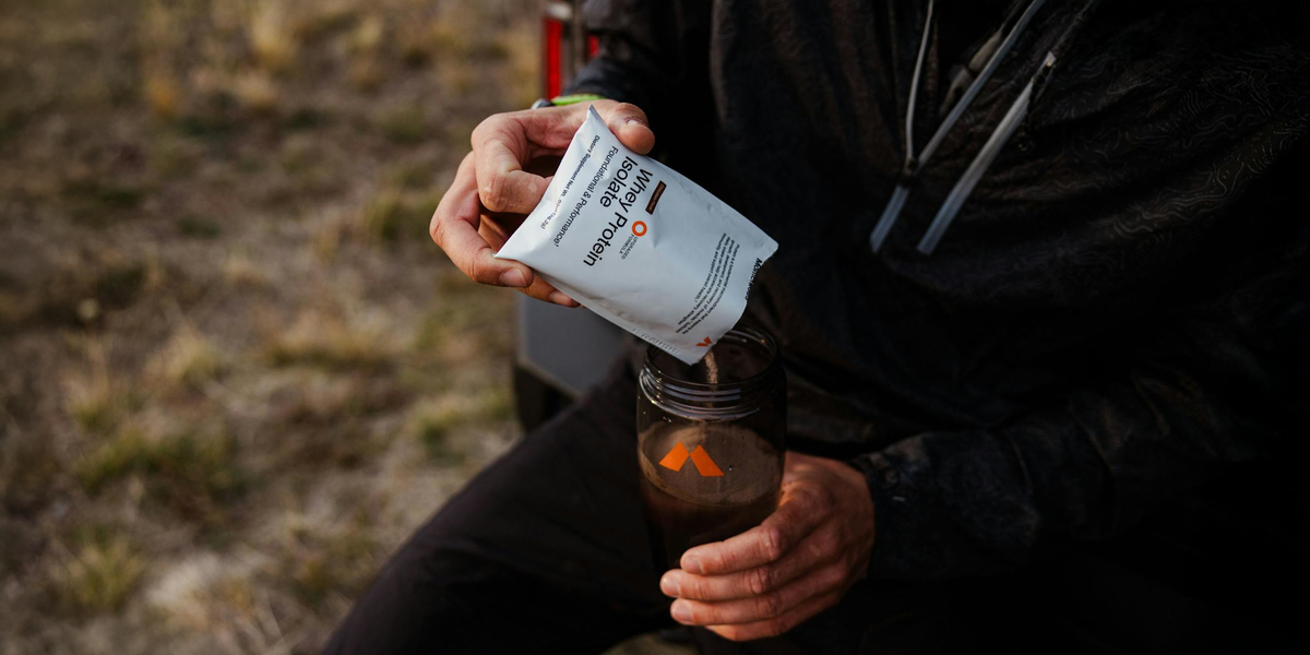 A man pours a travel pack of Momentous Whey Protein into a shaker bottle