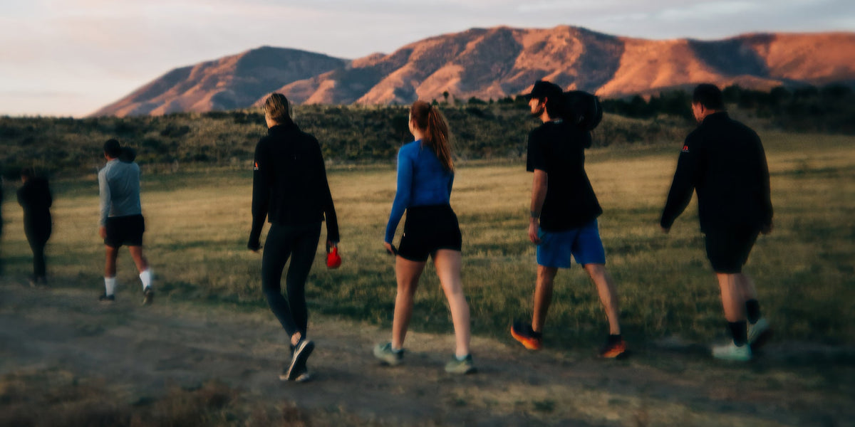 A group of men and women walk across a field on a morning hike