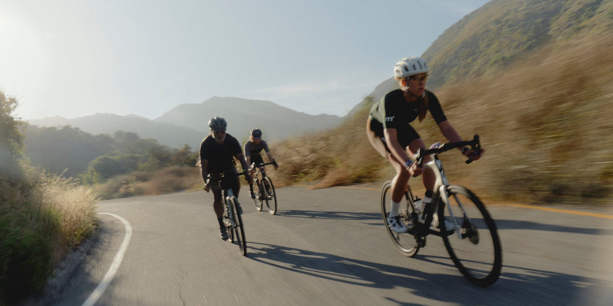three cyclists ride down a paved road in the mountains