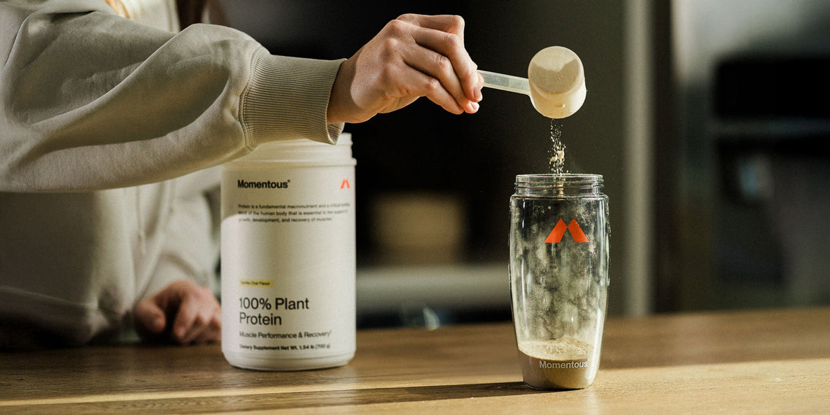 A person drops a scoop of protein powder into a shaker