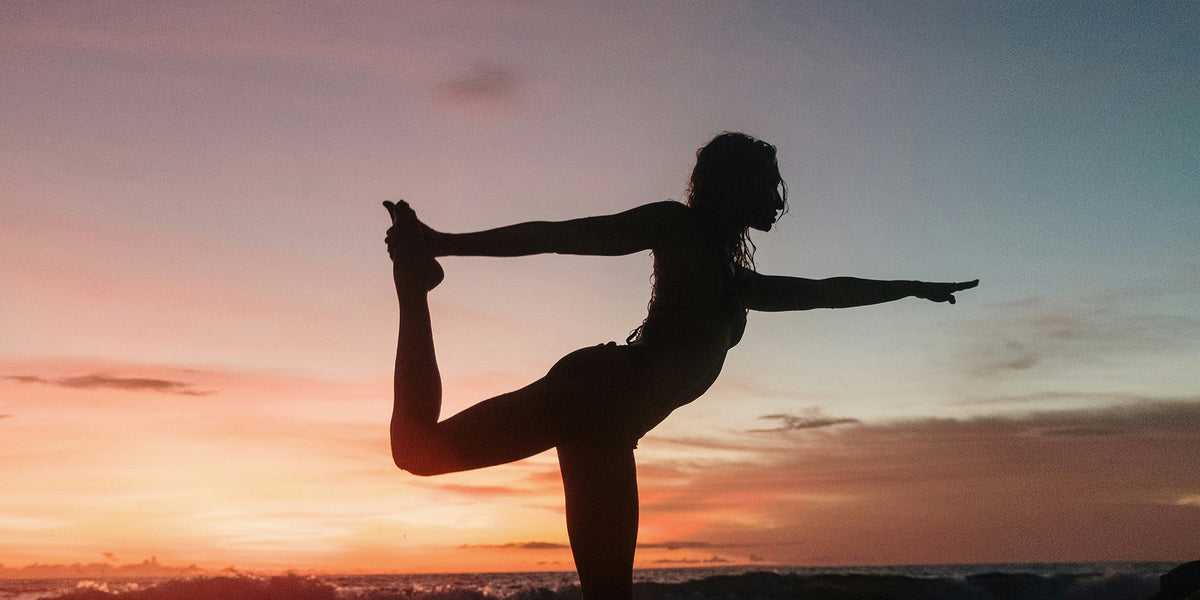 a woman performs a yoga move at sunset
