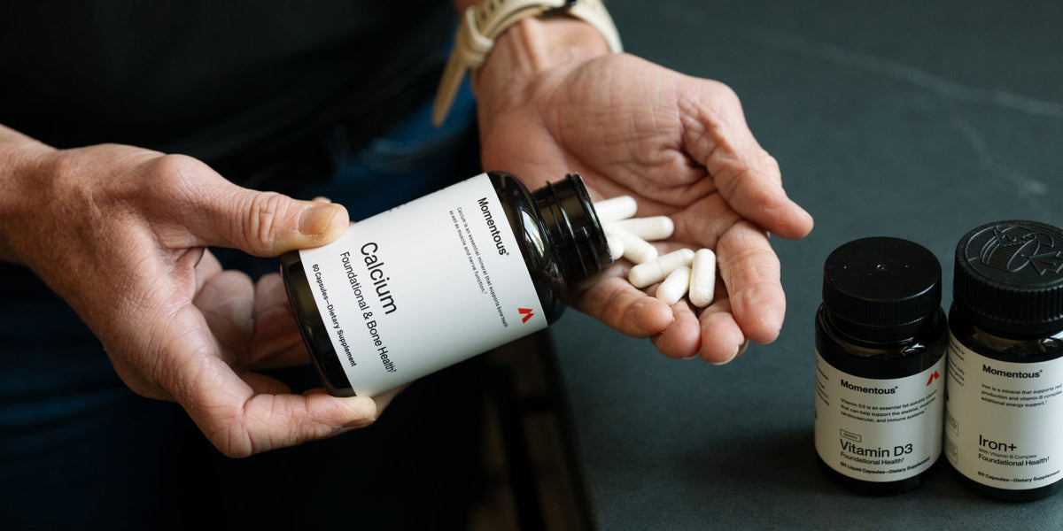 a woman's hand holds some Momentous Calcium capsules with Vitamin D3 and Iron also in shot