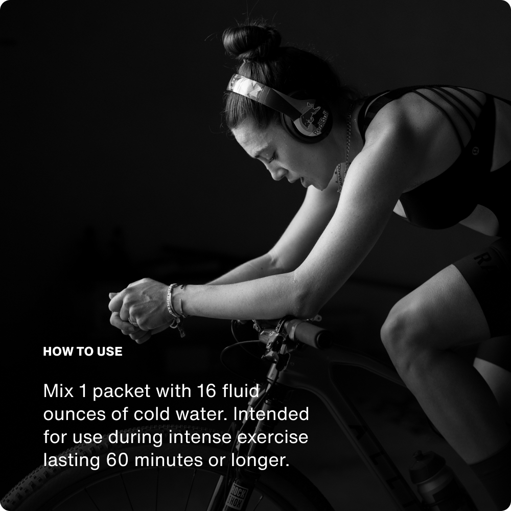 Black-and-white photo of a woman wearing headphones while riding an indoor bike trainer, leaning forward in an intense workout. White text on the left side reads: 'HOW TO USE — Mix 1 packet with 16 fluid ounces of cold water. Intended for use during intense exercise lasting 60 minutes or longer.