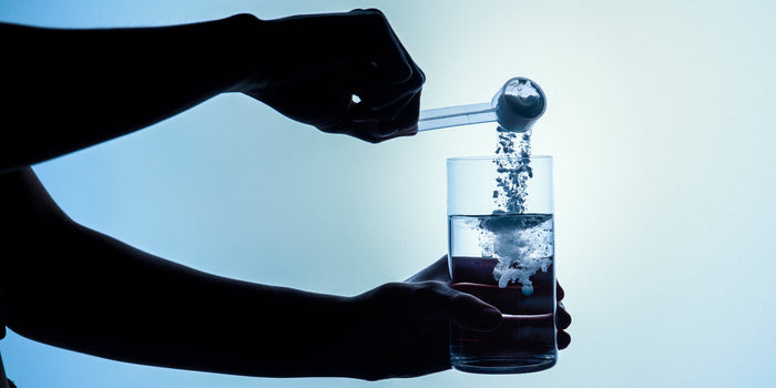 a person drops a scoop of creatine into a glass of water