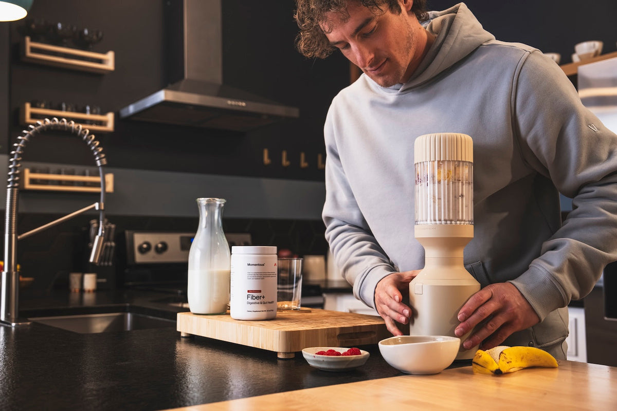 A male athlete makes a smoothie using a blender and Momentous Fiber+ and milk