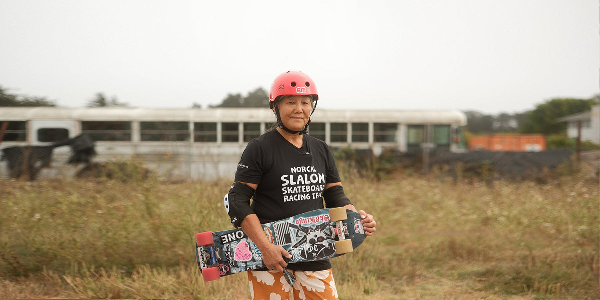 A woman wearing a skate helmet looks at the camera holding her skateboard