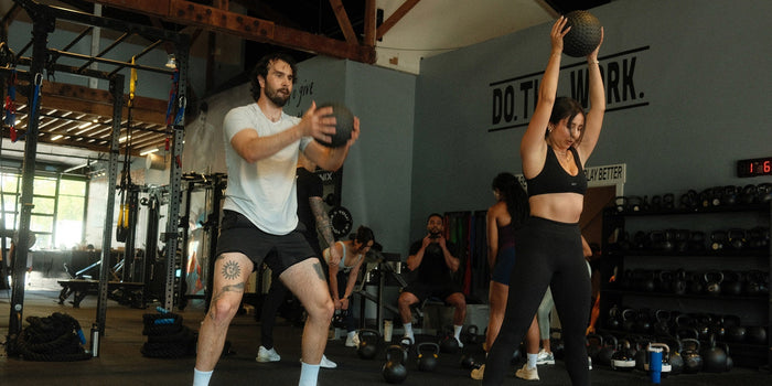 A man and woman in a gym doing medicine ball slams