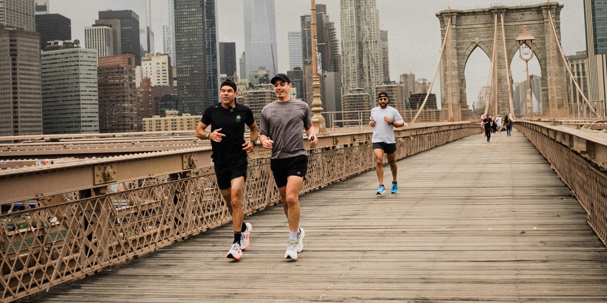 two male athletes run over a New York bridge with more athletes behind them