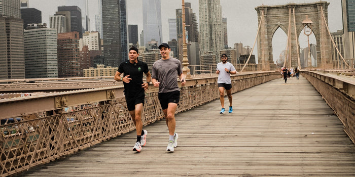 two male athletes run over a New York bridge with more athletes behind them