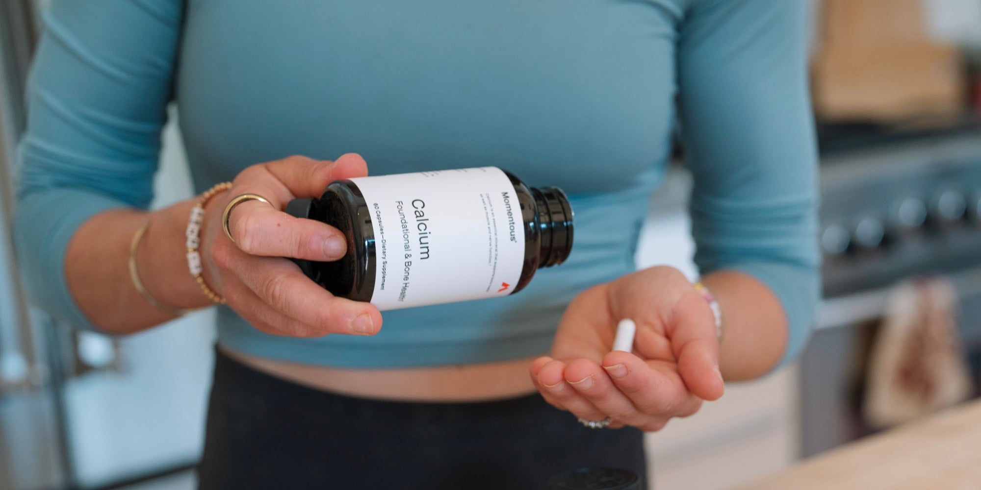 A woman holds a bottle of Momentous calcium and has one capsule in her hand