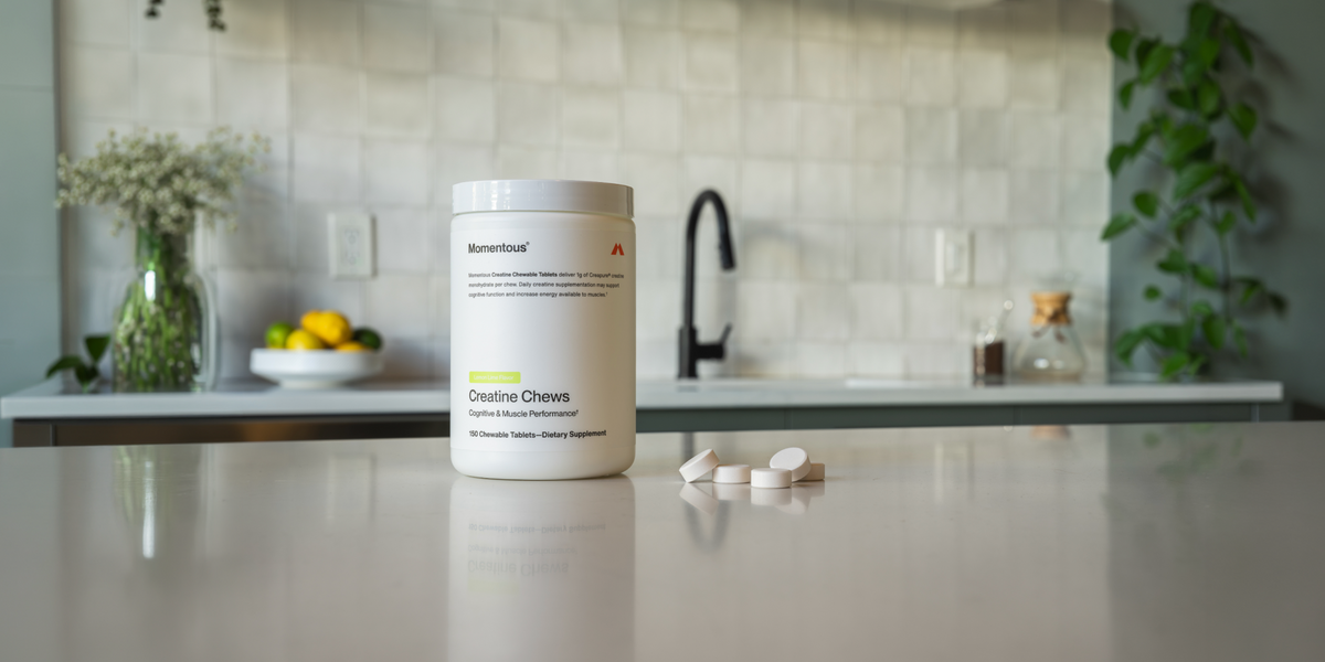 A tub of Momentous Creatine Chews sits on a kitchen countertop with a few chews pictured next to it