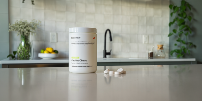 A tub of Momentous Creatine Chews sits on a kitchen countertop with a few chews pictured next to it