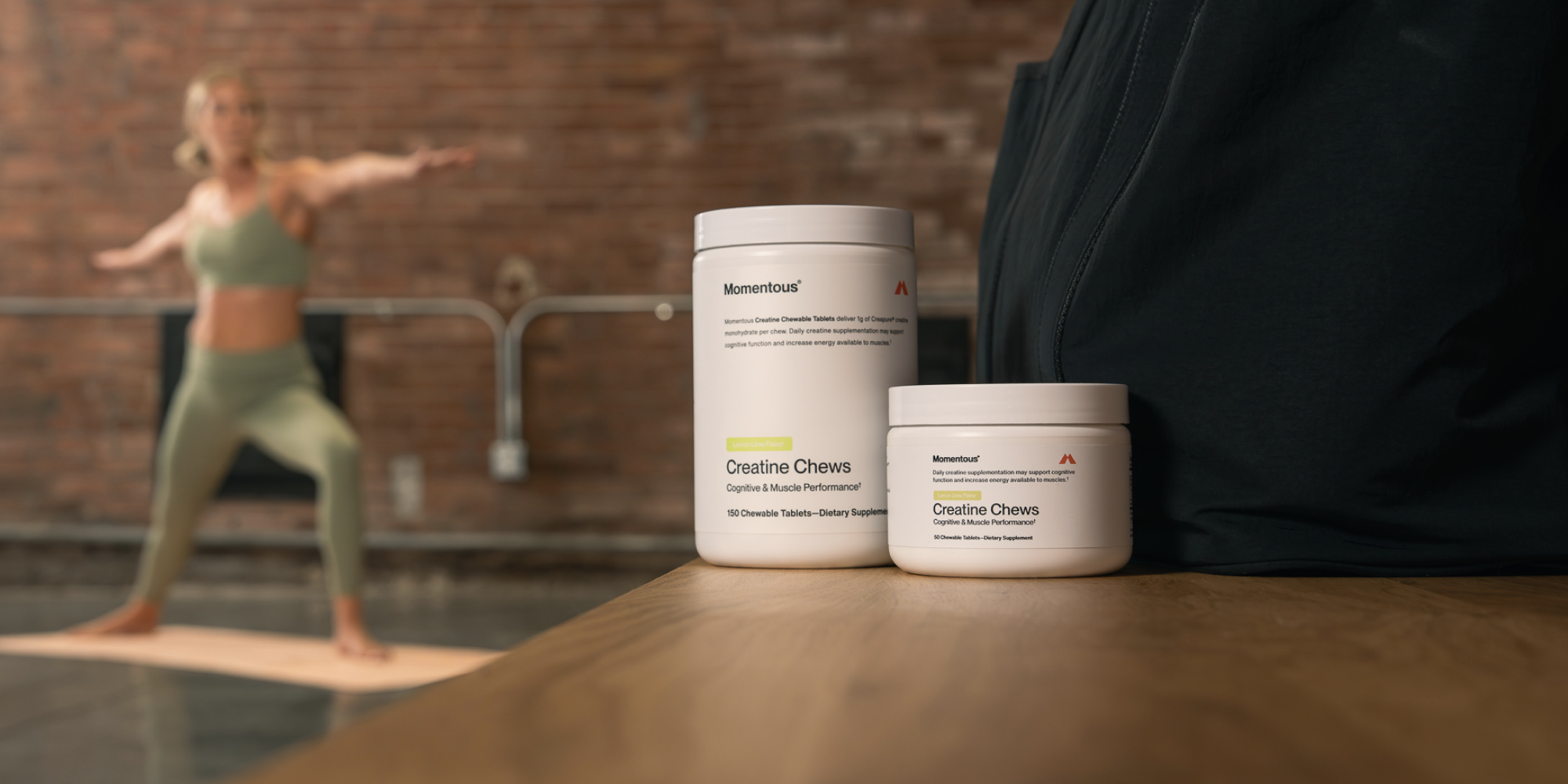 a woman does a yoga pose in the background with two tubs of creatine chews in the foreground