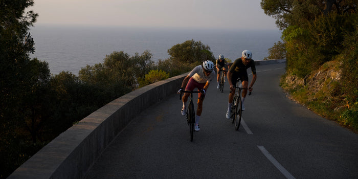 Three road cyclists race along a mountain road with the ocean in the background