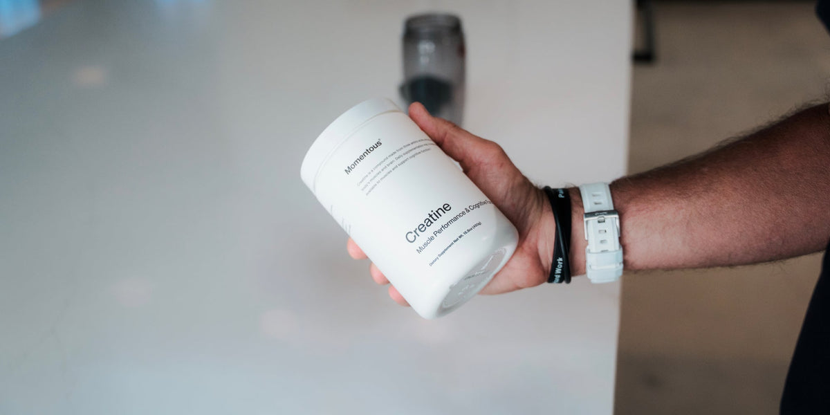 A tub of Momentous Creatine is held in a man's hand