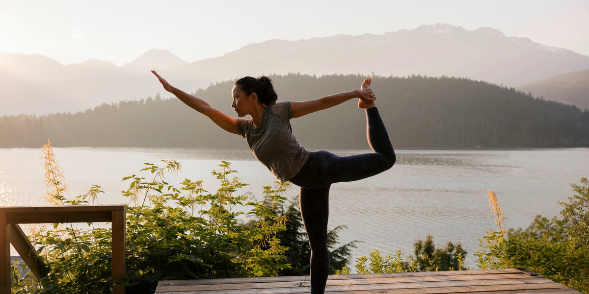 a young woman does a yoga pose in front of a lake and mountains