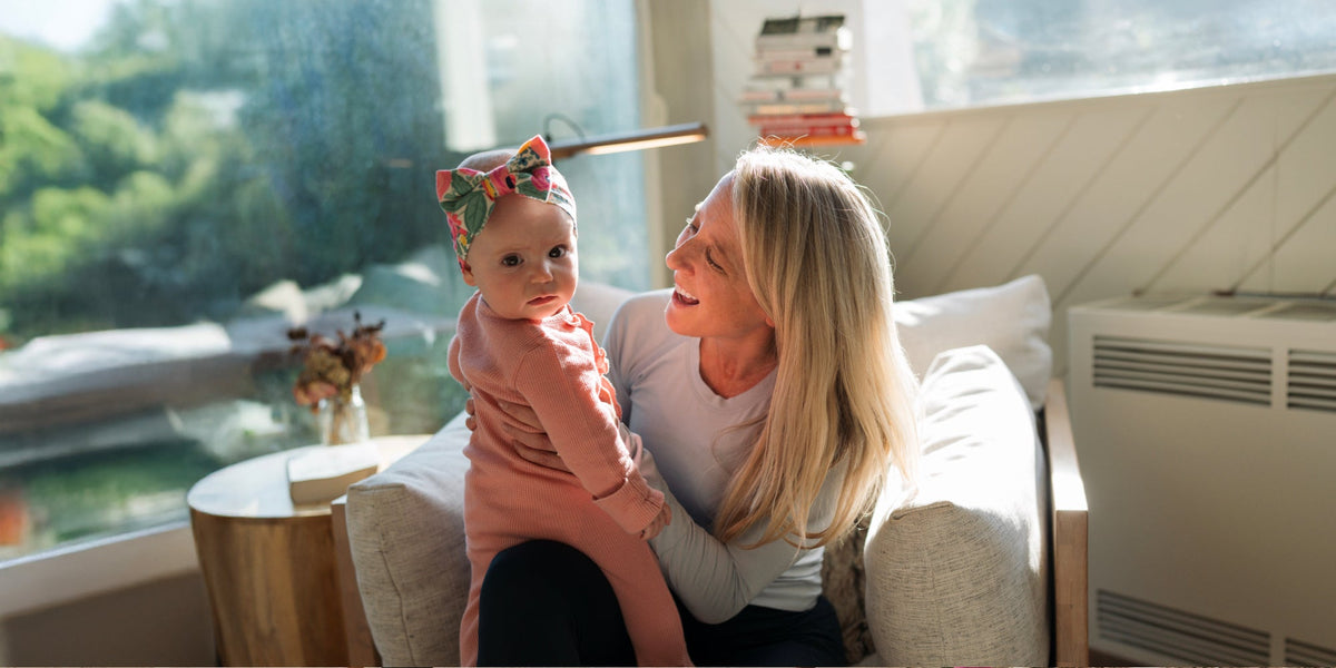 A baby girl looks at the camera with her mother looking at her smiling