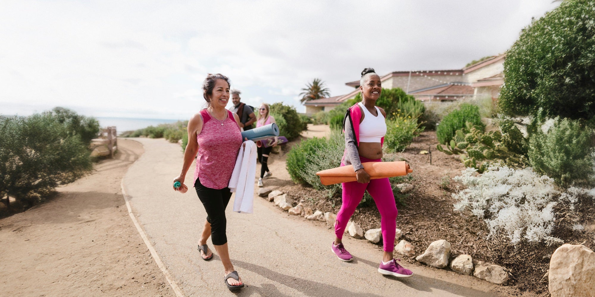 two older women walk along with yoga mats