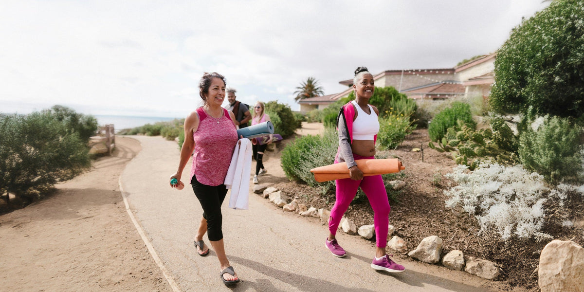 two older women walk along with yoga mats
