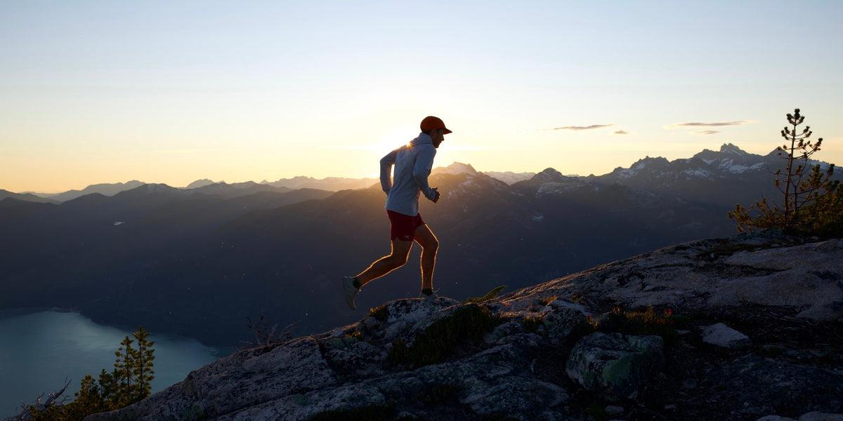 A male runner runs along a mountain trail with moutains in the backgroun