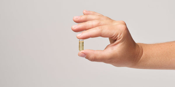 A person's hand holding a capsule of Vegan Omega-3