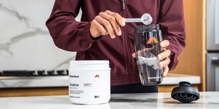 a tub of creatine with someone scooping it into a Momentous shaker