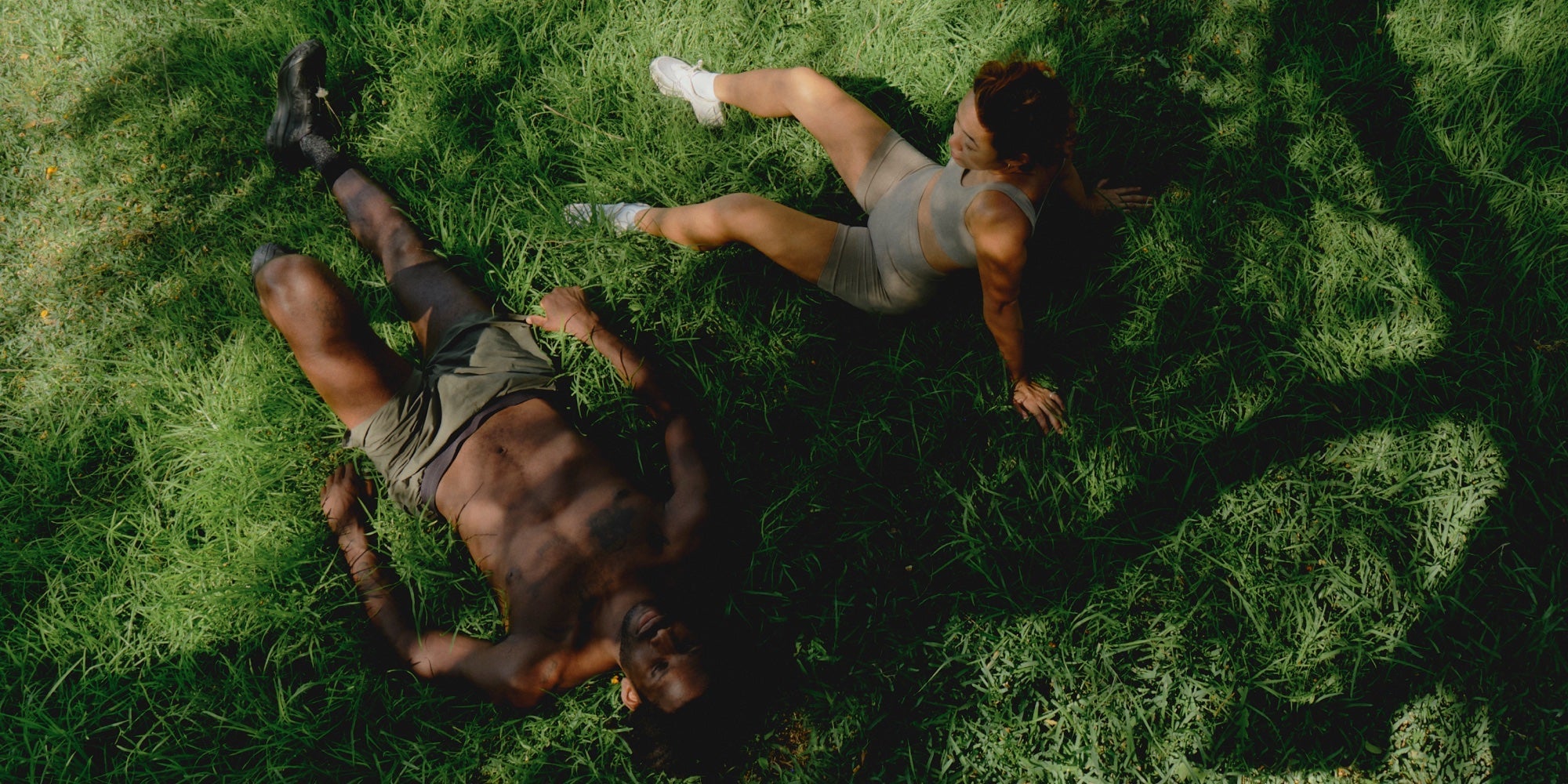 a male and female athlete lay on some grass after a workout