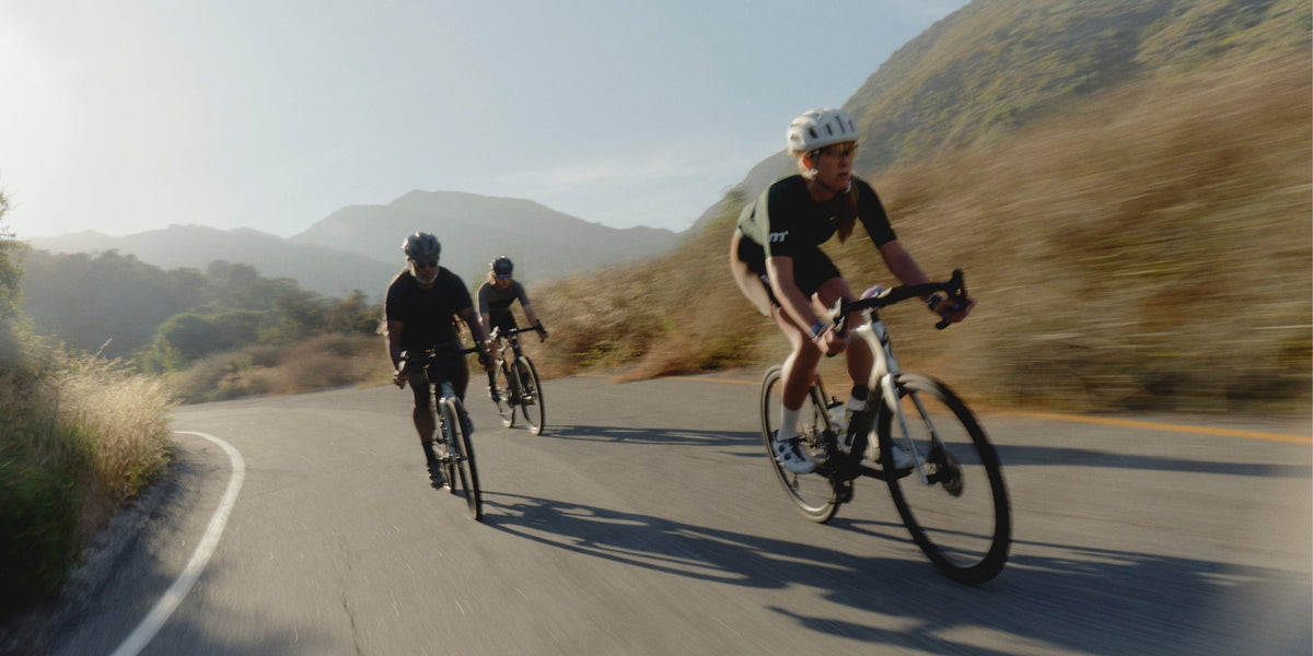 three cyclists ride down a paved road in the mountains