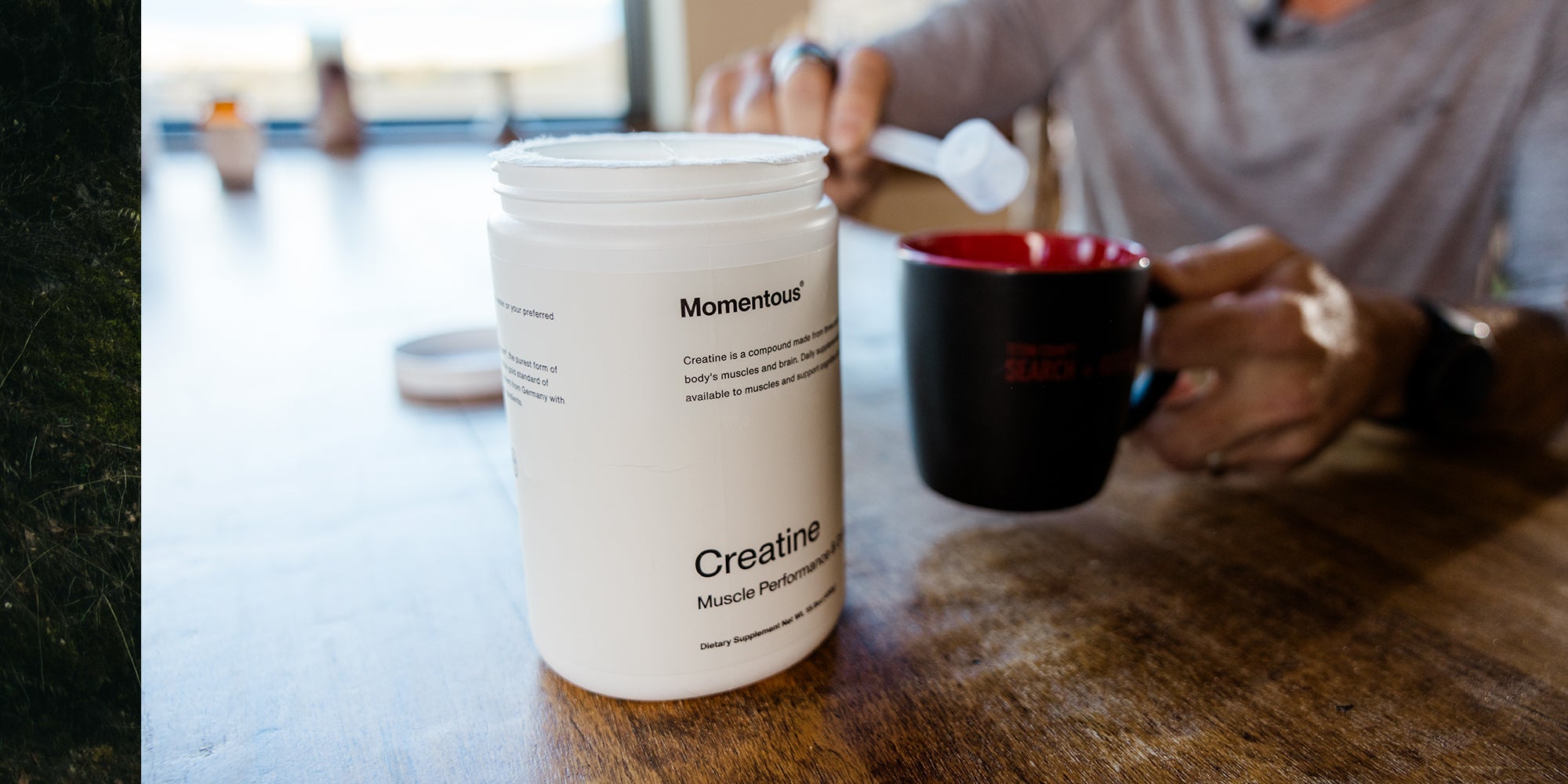 A tub of Momentous Creatine in front of a coffee mug