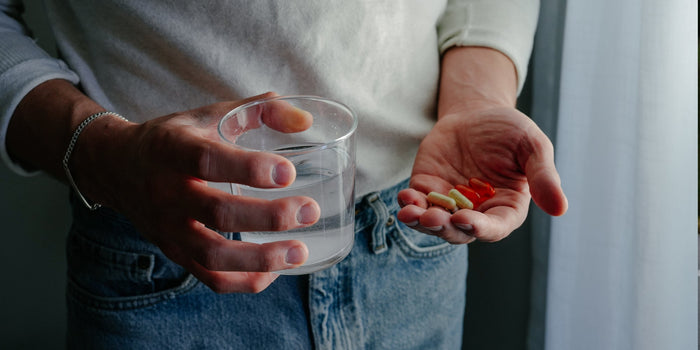A person holds a glass of water and some supplement capsules