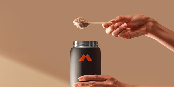 A person holding a scoop of protein powder over a shaker bottle