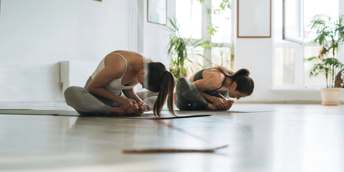two women do yoga poses on the floor