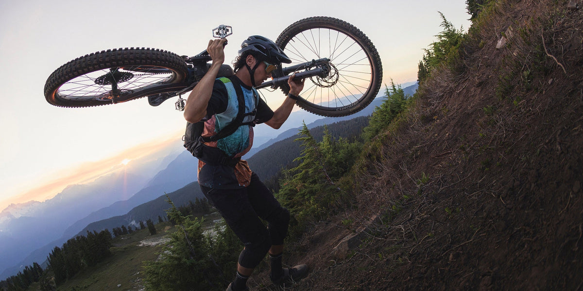 A man carries his mountain bike on his shoulder up a hill