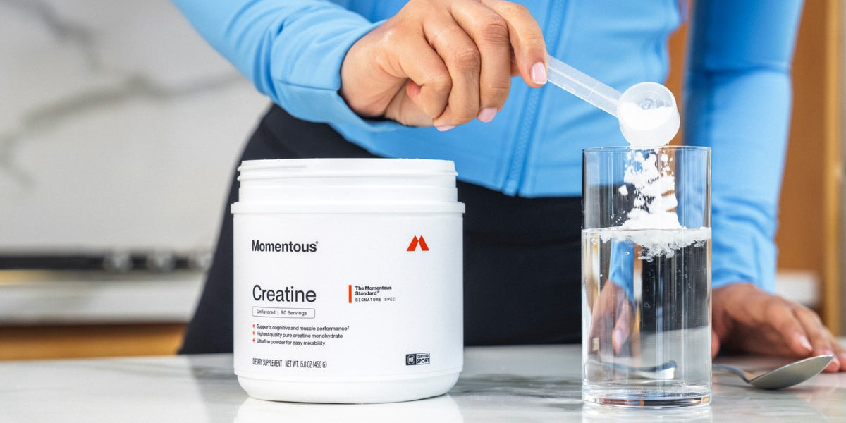 A woman scoops Momentous Creatine into a glass of water