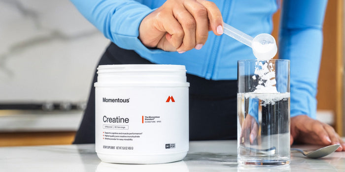 A woman scoops Momentous Creatine into a glass of water