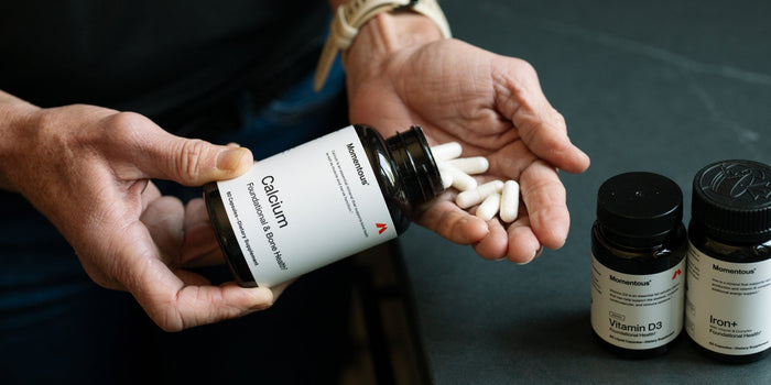 a woman's hand holds some Momentous Calcium capsules with Vitamin D3 and Iron also in shot