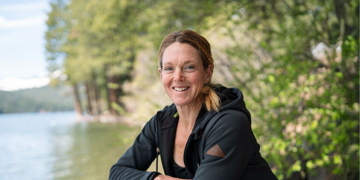 A portrait shot of Dr. Stacy Sims sat by a lake