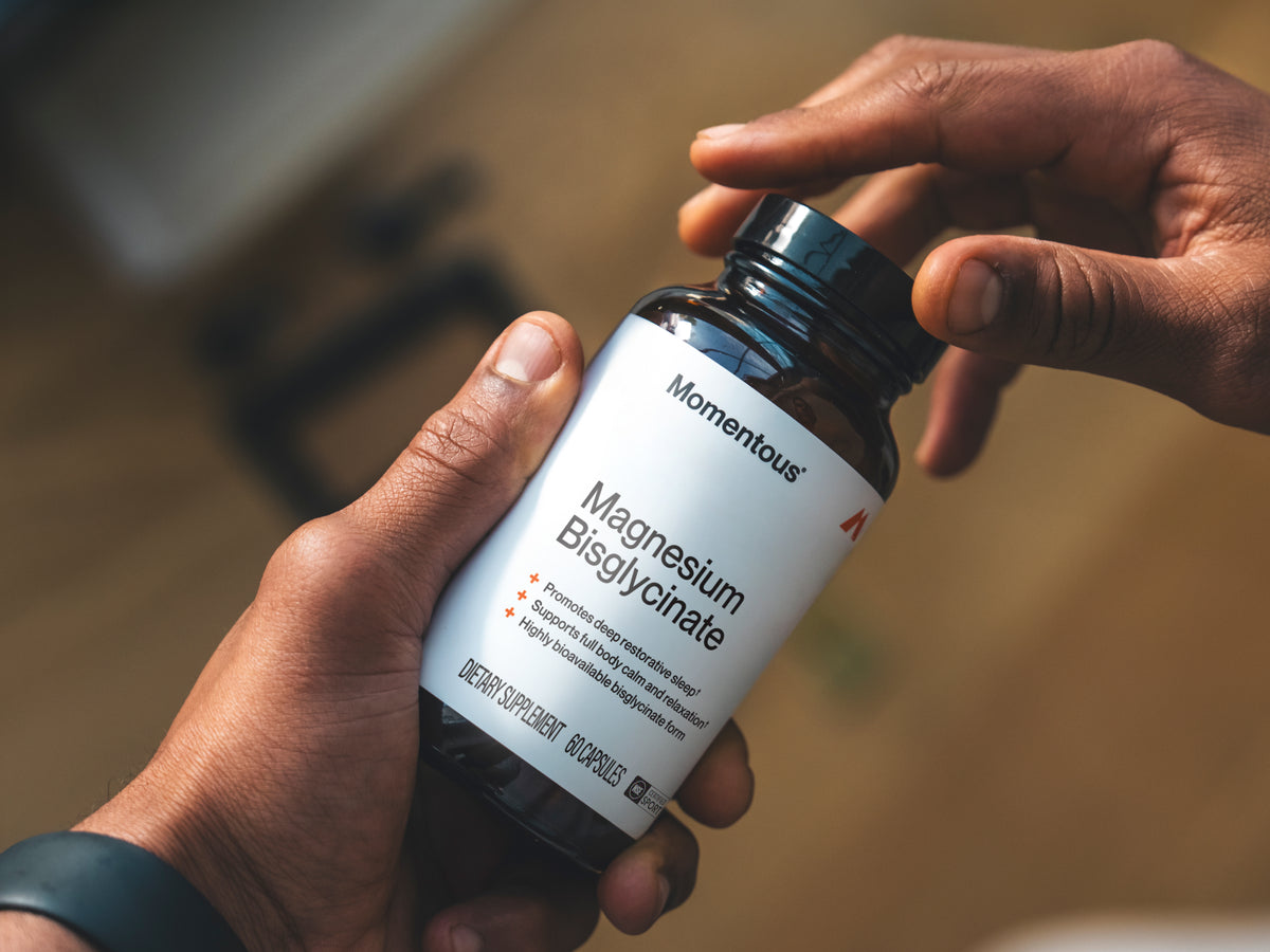 Hands opening a Momentous Magnesium Bisglycinate bottle, 60 capsules, labeled for deep restorative sleep and full-body calm.