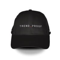 Black baseball cap with “TREND_PROOF” embroidered in white across the front, featuring a red underscore between the words.