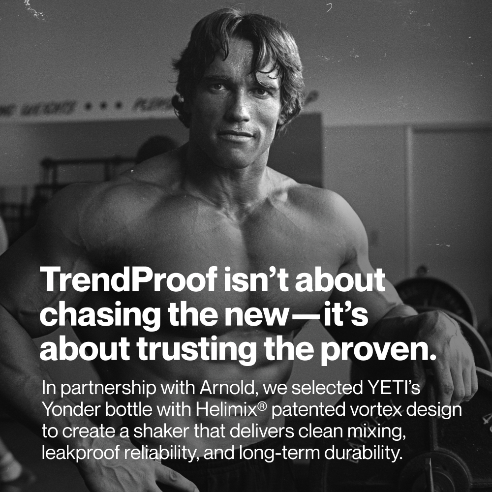 Black-and-white photo of Arnold Schwarzenegger in a gym setting, shown from the waist up with a muscular build and focused expression. Large white overlay text reads: “TrendProof isn’t about chasing the new—it’s about trusting the proven.” Smaller text below reads: “In partnership with Arnold, we selected YETI’s Yonder bottle with Helimix® patented vortex design to create a shaker that delivers clean mixing, leakproof reliability, and long-term durability.”