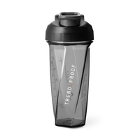 Front view of a transparent gray Helimix shaker bottle with a black lid and flip cap. The bottle has an angular, faceted design with measurement markings along the side and the word “HELIMIX” embossed vertically on the right side panel. Printed vertically on the front in white text is “TREND_PROOF” with an orange underscore between the words. The shaker is designed for clean mixing and everyday training use.