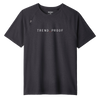 Front view of a charcoal gray short-sleeve performance T-shirt with raglan sleeves. The shirt features a minimalist design with the word “TREND_PROOF” printed in clean white uppercase lettering across the chest, with a subtle red underscore between the words. A small stitched emblem detail appears near the left shoulder seam. The collar label reads “RHONE.” The fabric appears lightweight and athletic with a smooth, structured drape.