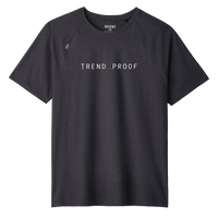 Front view of a charcoal gray short-sleeve performance T-shirt with raglan sleeves. The shirt features a minimalist design with the word “TREND_PROOF” printed in clean white uppercase lettering across the chest, with a subtle red underscore between the words. A small stitched emblem detail appears near the left shoulder seam. The collar label reads “RHONE.” The fabric appears lightweight and athletic with a smooth, structured drape.