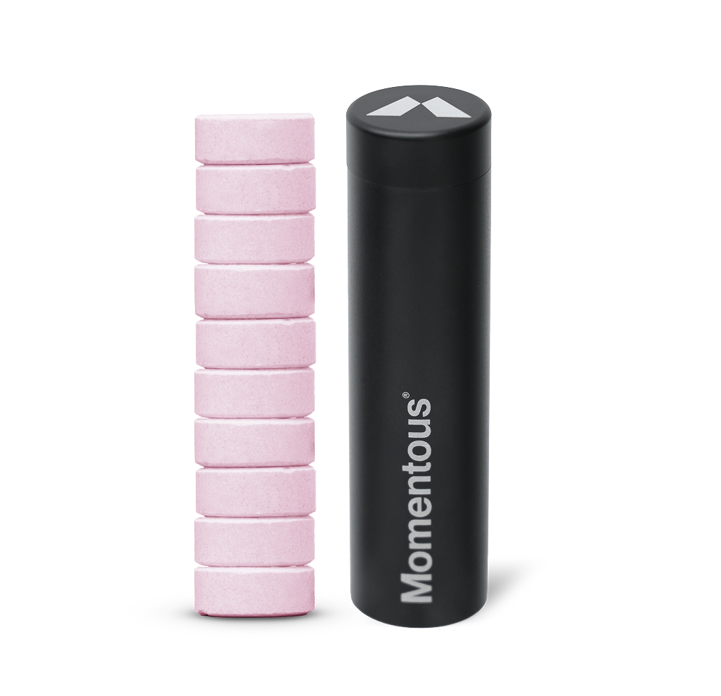 Stack of pink creatine chew tablets beside a black Momentous travel tube
