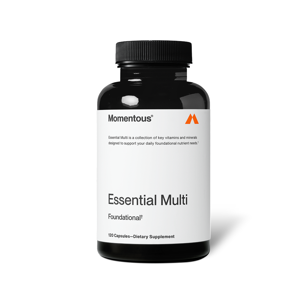 Black bottle of Momentous Essential Multi capsules centered on a transparent background. Text on the label reads: “Momentous®” “Essential Multi is a collection of key vitamins and minerals designed to support your daily foundational nutrient needs.*” “Essential Multi” “Foundational†” “120 Capsules—Dietary Supplement”