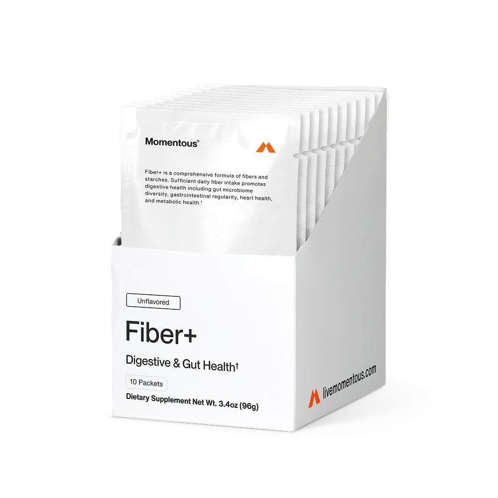 Box of Momentous Fiber+ packets displayed open with individual sachets inside. Packaging reads: “Momentous,” “Fiber+ is a comprehensive formula of fibers and starches. Sufficient daily fiber intake promotes digestive health including gut microbiome diversity, gastrointestinal regularity, heart health, and metabolic health†.” Front of box reads: “Unflavored,” “Fiber+,” “Digestive & Gut Health†,” “10 Packets,” “Dietary Supplement Net Wt. 3.4 oz (96g),” and “livemomentous.com.”