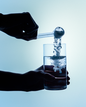 Hand pouring Momentous Creatine powder from a scoop into a clear glass of water representing exceptional mixability, achieved through a superior micronization process that creates ultra-fine creatine powder that mixes seamlessly with no grit left behind