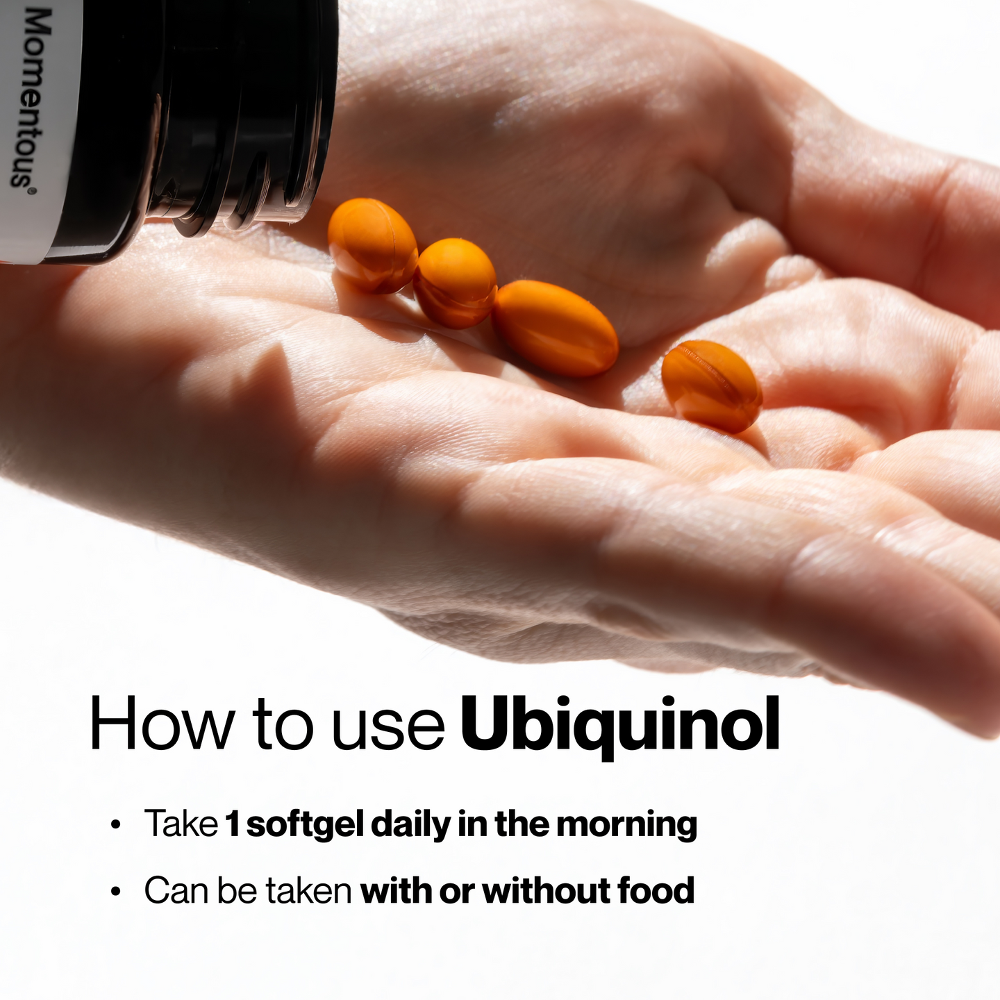 Close-up of a hand holding four orange softgel capsules, with a black Momentous bottle tipped above it. Text: How to use Ubiquinol, Take 1 softgel daily in the morning, Can be taken with or without food.