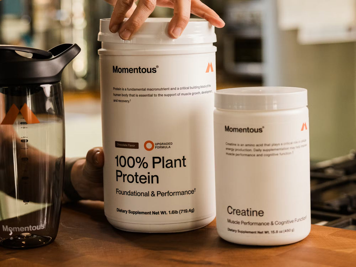 Two containers of Momentous protein and creatine on a wooden surface.