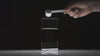 Hand holding a clear measuring scoop pouring Momentous Signature Spec Creatine into a glass of water on a black background, showing superior mixability and clean dissolution with no grit or clumping